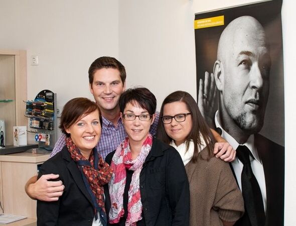 Vier freundliche Menschen stehen in einem modernen Büro neben einem großen Schwarz-Weiß-Porträt.