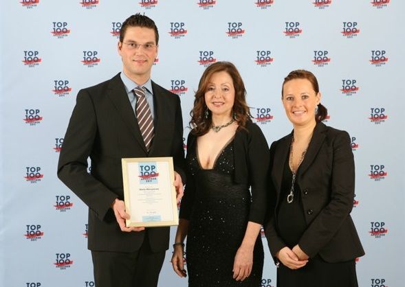 Drei Personen in Businesskleidung posieren bei einer Top 100 Auszeichnung für Innovation.